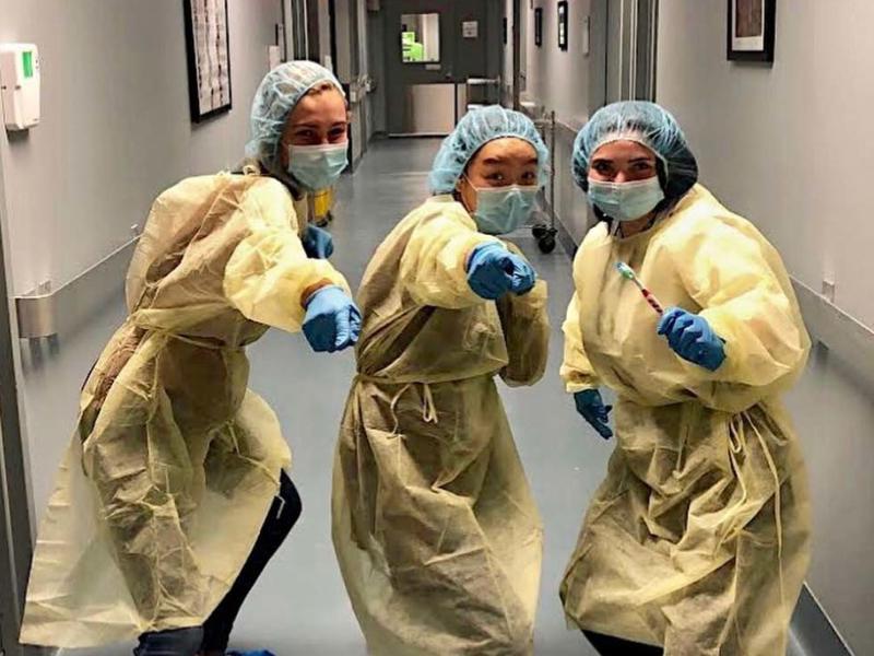 3 young women dressed in surgical scrubs in a hospital hallway, pointing at the viewer