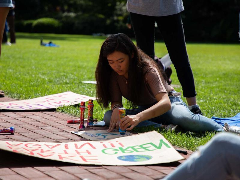 Young woman works on a poster for a climate march on a sunny day