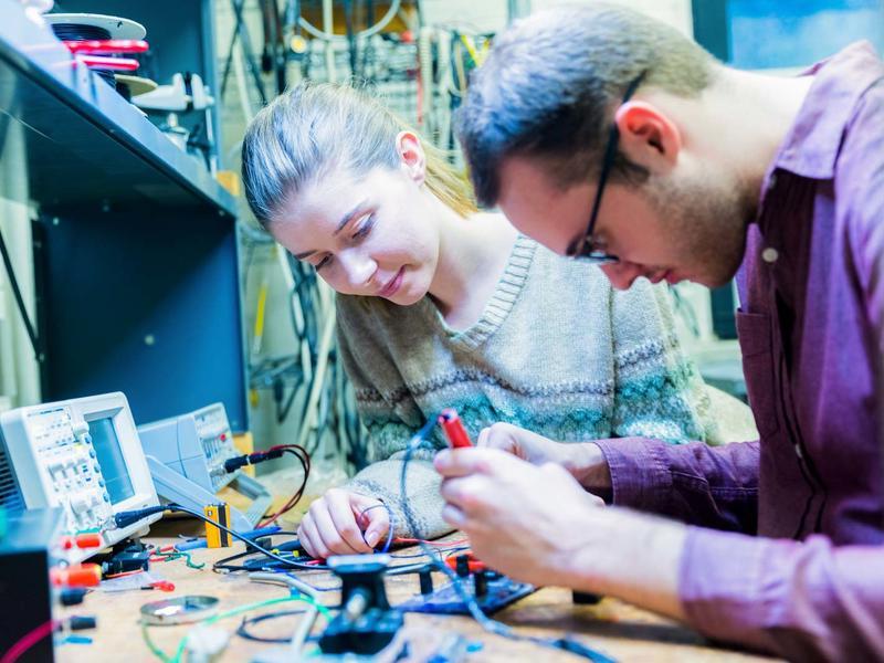 Man and woman working at an electronics bench with engineering tools
