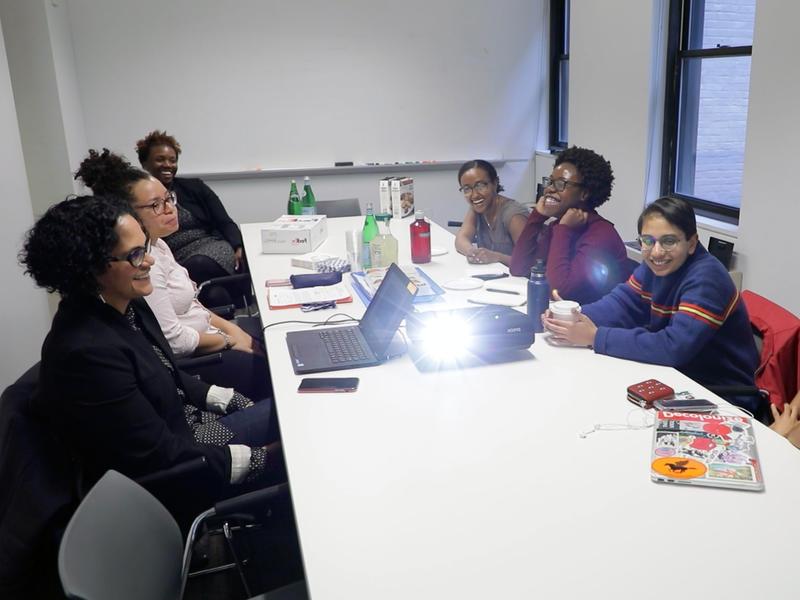 half a dozen women of color sit around a conference table